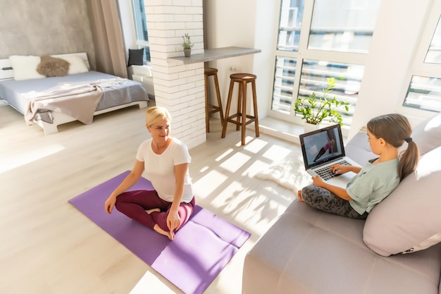 Jonge volwassen moeder met haar dochter die thuis samen naar online training kijkt, op zoek naar een laptop