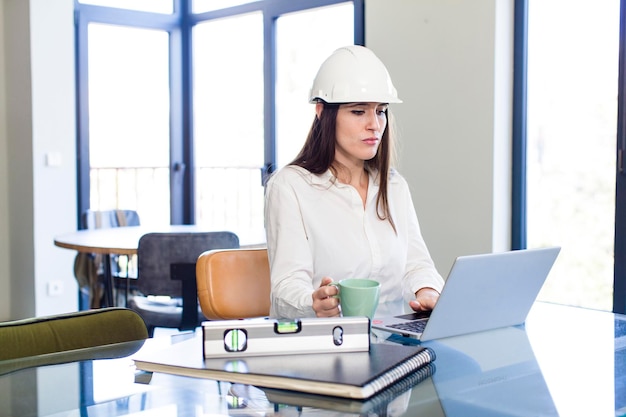 Jonge volwassen mooie architectenvrouw die op kantoor met laptop werkt