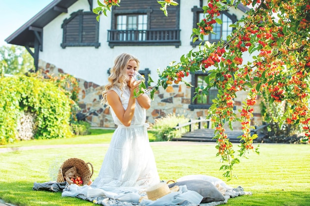 Foto jonge volwassen mooie blonde in een witte jurk een wijnglas in haar hand in de tuin onder