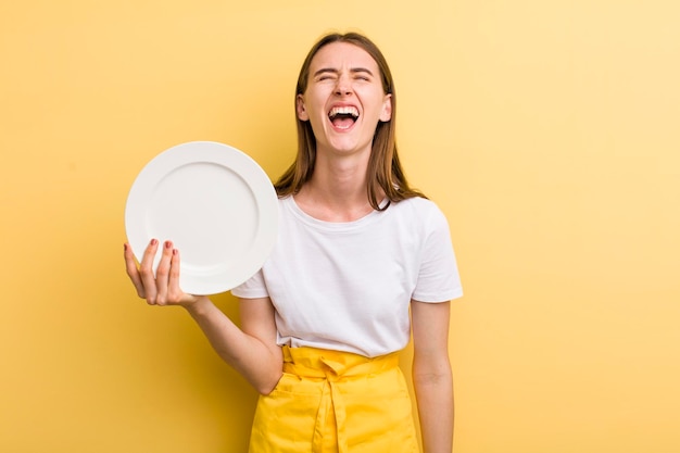 Jonge volwassen mooie chef-kokvrouw die een leeg bord houdt