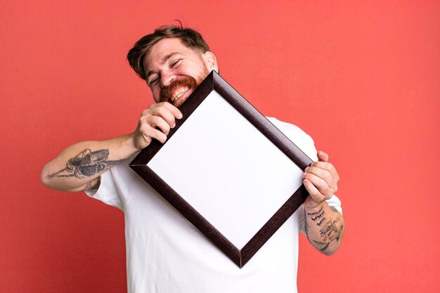 Jonge volwassen rood haar bebaarde coole man met een leeg fotolijstje