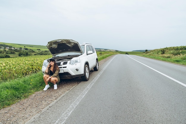 Jonge volwassen vrouw die in de buurt van een kapotte auto op de snelweg staat en praat