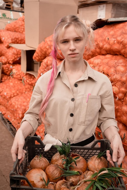 Jonge volwassen vrouw die in het magazijn werkt en uienbollen voorbereidt voor het kweken van groen in het voorjaar in