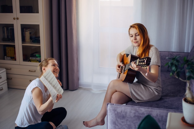 Jonge volwassen vrouw houdt muzieknotitieboekje vast en kijkt naar haar vriend die gitaar speelt. twee schattige meisjes spelen thuis muziek. vriendschap, liefde, familie vrije tijd, hobby's.