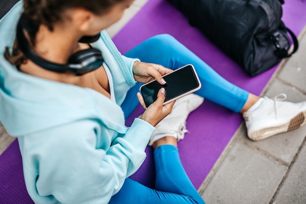 Jonge volwassen vrouw rust na fitnesstraining. Ze zit en gebruikt haar smartphone om met iemand te communiceren.