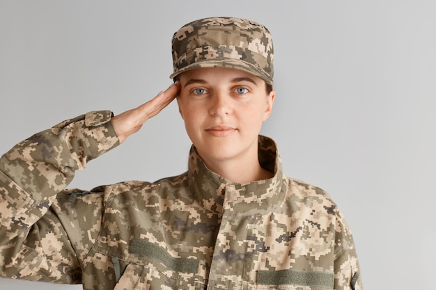 Jonge volwassen vrouw soldaat die met de hand in de buurt van het hoofd salueert, naar de camera kijkt met een aangename gezichtsuitdrukking, een militair uniform draagt, blij is om in het leger te dienen.