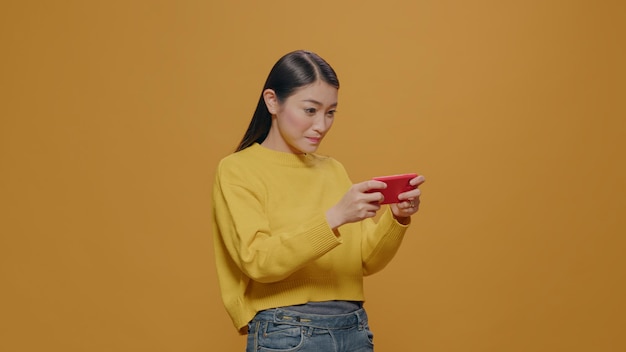 Jonge volwassene die online games speelt op mobiele telefoon, geniet van vrijetijdsbesteding. Aziatische vrouw die smartphone gebruikt om plezier te hebben met virtueel spel op elektronisch apparaat. Persoon met smartphone.