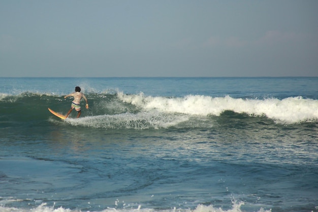 Jonge volwassenen die golven vangen tijdens het surfen op het strand van pangandaran op een bewolkte dag op helderblauw water