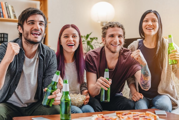 Jonge vrienden die bier drinken en popcorn eten en juichen voor sportspel