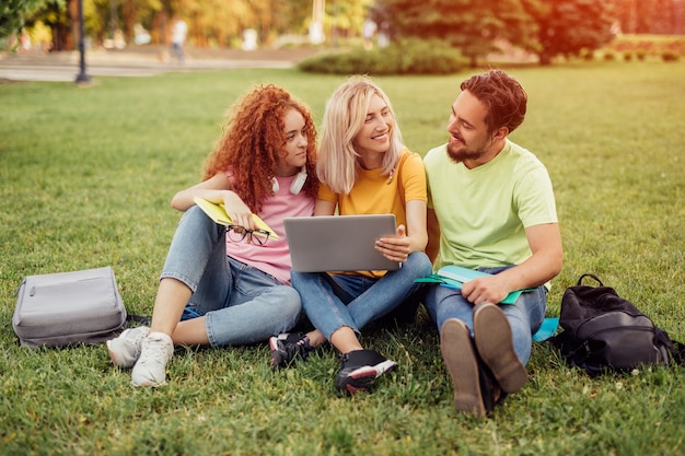 Jonge vrienden die op gras zitten en laptop gebruiken voor huiswerk