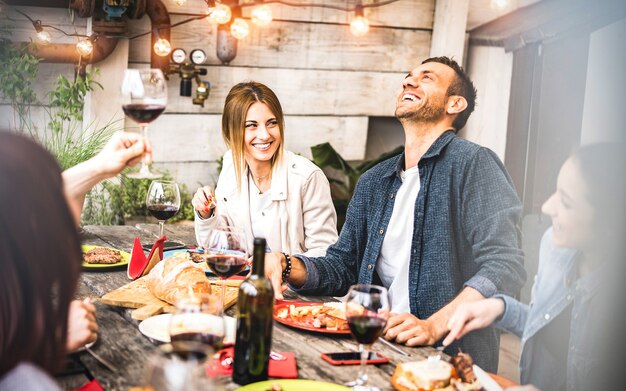 Jonge vrienden die plezier hebben met het drinken van rode wijn op het balkon op het huisdinerfeest