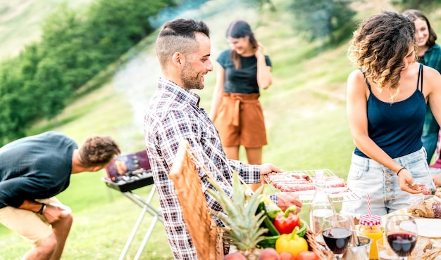 Jonge vrienden die plezier hebben op een picknick in de buitenlucht die voedsel bereiden op een barbecue-grillfeest