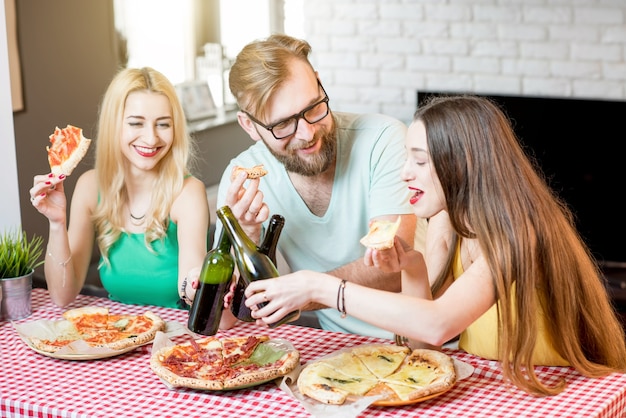 Jonge vrienden, nonchalant gekleed in kleurrijke t-shirts, lunchen met pizza en bier thuis