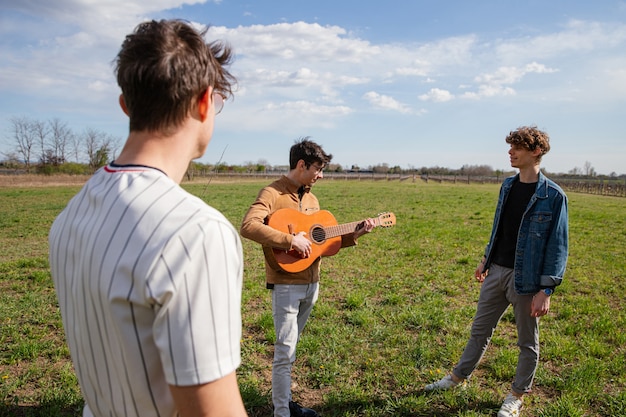 Jonge vrienden ontmoeten elkaar in een weiland in de open lucht met een gitaar en zingen liedjes - mannelijke vriendschap en passie voor muziekconcept - focus op gitaar.