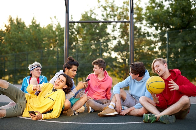 Jonge vrienden zittend op een basketbalveld, ontspannen en pauze nemen na de wedstrijd