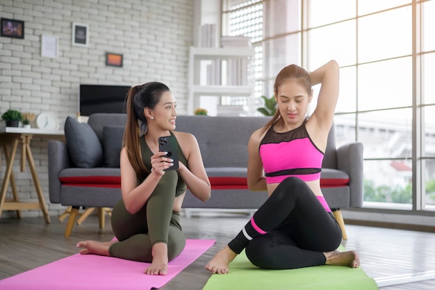 Jonge vriendenvrouwen die thuis yoga beoefenen met behulp van een smartphone via online les