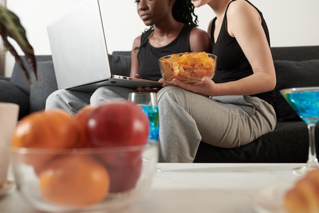 Jonge vriendinnen die chips eten bij het kiezen van een show op laptop