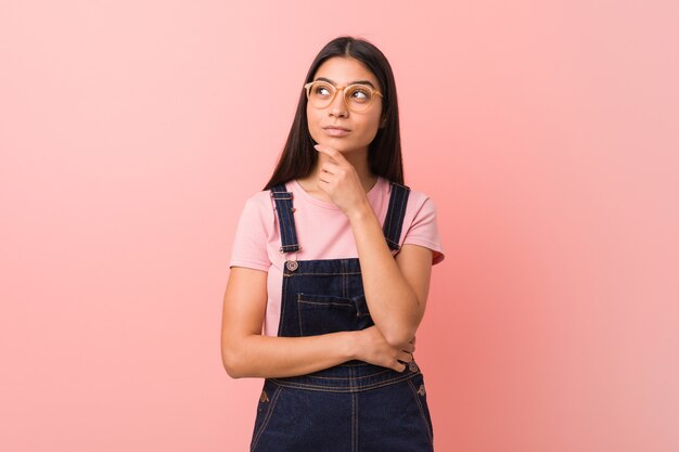 Jonge vrij arabische vrouw die een jeans dungaree draagt die zijwaarts met twijfelachtige en sceptische uitdrukking kijkt.