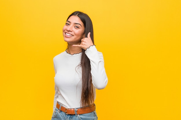 Jonge vrij Arabische vrouw tegen een geel die een mobiel telefoongesprekgebaar met vingers tonen.