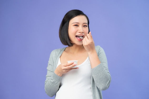 Jonge vrij Aziatische zwangere vrouw die yoghurt eet