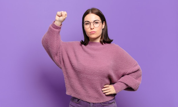 Jonge vrij casual vrouw die zich serieus, sterk en rebels voelt, vuist opstekend, protesteert of vecht voor revolutie