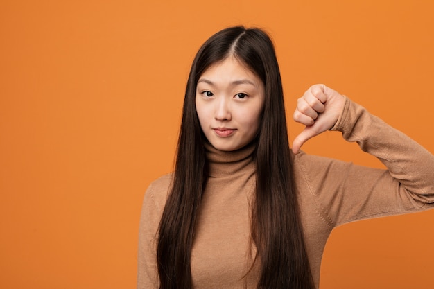 Jonge vrij Chinese vrouw die een afkeergebaar, duimen neer tonen. Meningsverschil concept.