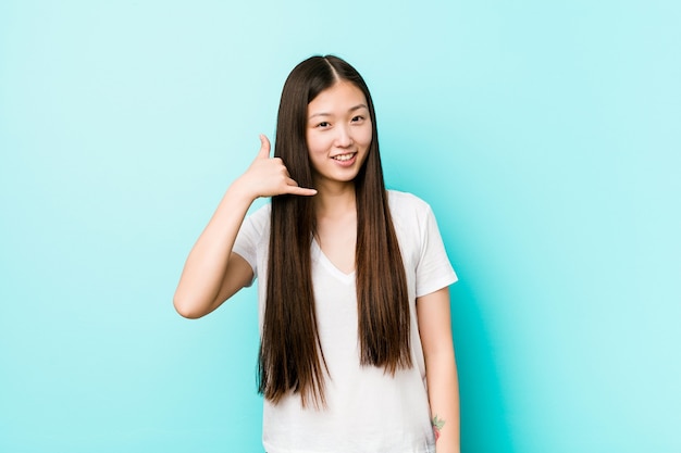 Jonge vrij chinese vrouw die een mobiel telefoongesprekgebaar met vingers toont.