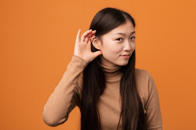 Jonge vrij chinese vrouw die een roddel probeert te luisteren.