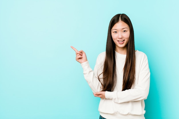 Jonge vrij chinese vrouw glimlachend vrolijk wijzend met wijsvinger weg.