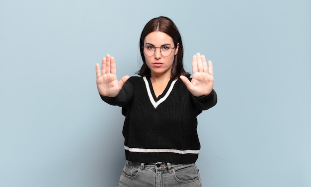 Jonge, vrij informele vrouw die ernstig, ongelukkig, boos en ontevreden kijkt en de toegang verbiedt of stop zegt met beide open handpalmen