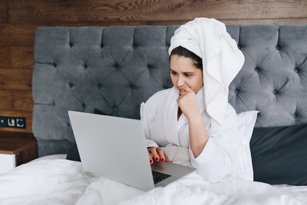 Jonge vrij Kaukasische onderneemster die aan haar laptop in haar bed werkt