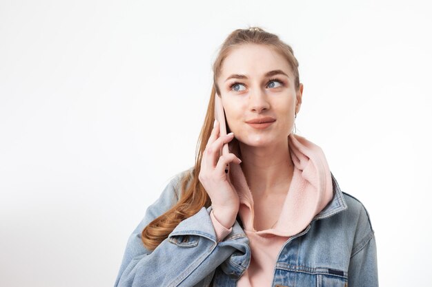 Jonge vrij kaukasische vrouw die op telefoon spreekt die op witte achtergrond wordt geïsoleerd