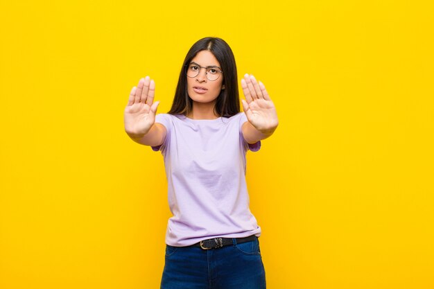 Jonge vrij latijnse vrouw die ernstig met beide open palmen tegen vlakke muur kijkt