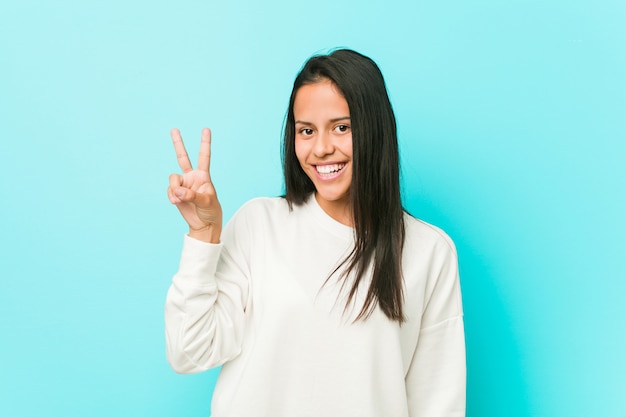 Jonge vrij Spaanse vrouw blij en onbezorgd tonend een vredessymbool met vingers.