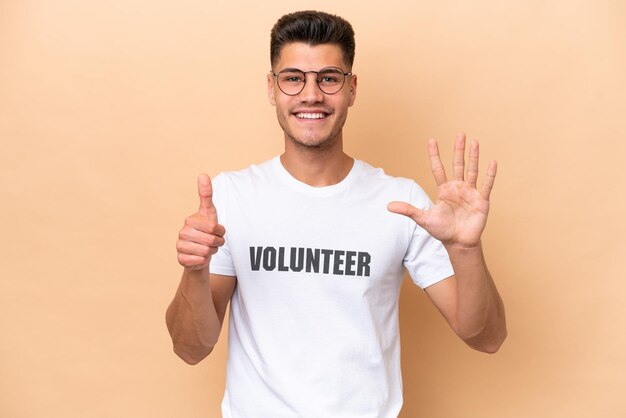 Jonge vrijwilliger blanke man geïsoleerd op beige achtergrond zes tellen met vingers