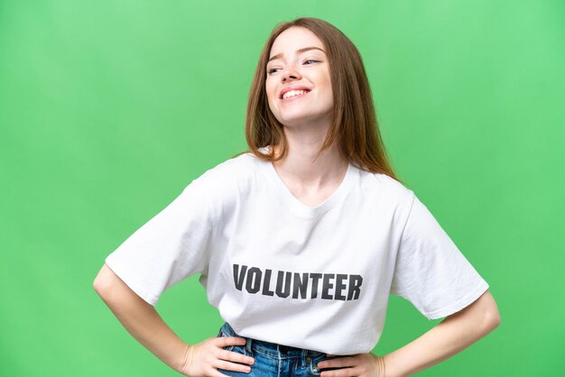 Jonge vrijwilliger vrouw over geïsoleerde chroma key achtergrond poseren met armen op heup en glimlachen