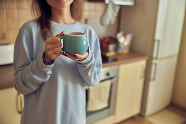 Jonge vrolijke en gelukkige vrouw bereidt smakelijke thee thuis in haar keuken