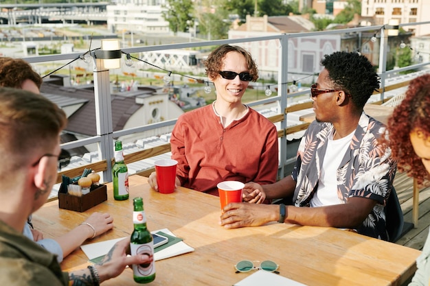 Jonge vrolijke interraciale mannen en hun vriendinnen chatten aan tafel in café