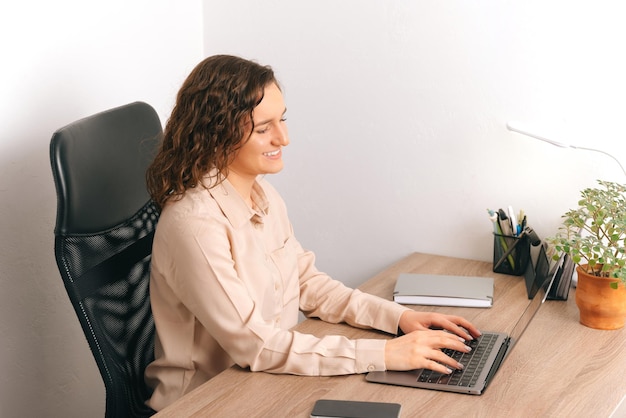 Jonge vrolijke kortharige vrouw zit aan het bureau, ze werkt aan de laptop