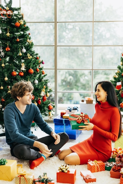 Jonge vrolijke paar in kerstmutsen met behulp van tablet zitten omringd door kleurrijke geschenkdozen genieten van het vieren van Kerstmis thuis.
