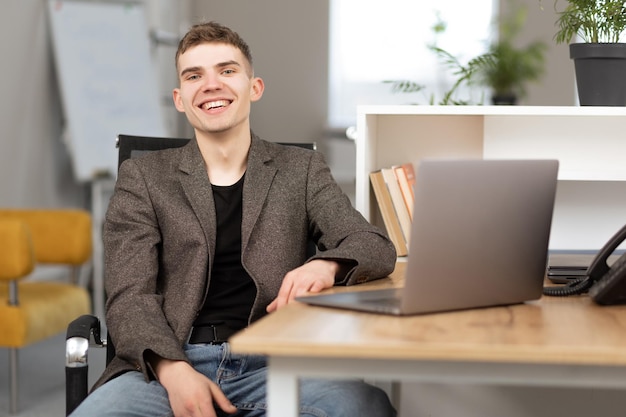 Jonge vrolijke programmeur die op kantoor op laptop werkt
