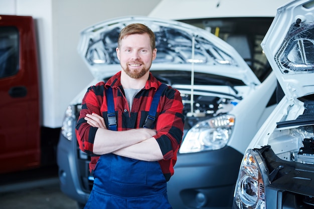 Jonge vrolijke reparateur of technicus in werkkleding die zijn armen kruist