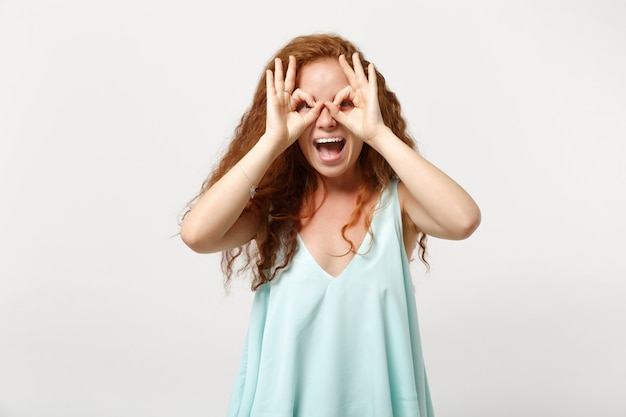 Jonge vrolijke roodharige vrouw in casual lichte kleding poseren geïsoleerd op een witte muur achtergrond. Mensen levensstijl concept. Bespotten kopie ruimte. Handen vasthouden in de buurt van ogen, een bril of verrekijker imiteren.