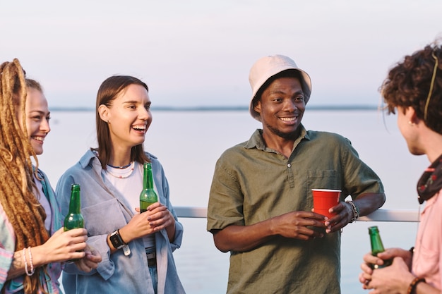 Jonge vrolijke vrienden met drankjes die grappen vertellen op het zomerfeest