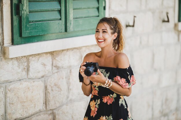 Jonge vrolijke vrouw die foto's maakt met haar digitale camera terwijl ze een mediterrane stad verkent.