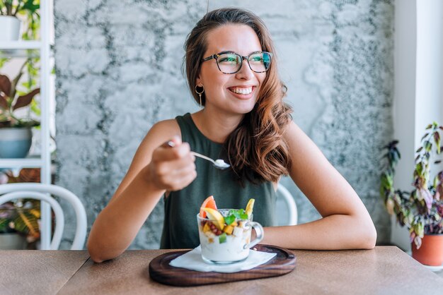 Jonge vrolijke vrouw die fruitsalade eet.