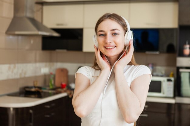 Jonge vrolijke vrouw die naar muziek luistert met een koptelefoon in de woonkamer