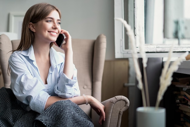 Jonge vrolijke vrouw die op mobiele telefoon thuis spreekt