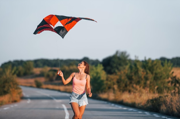 Jonge vrolijke vrouw die plezier heeft met vlieger buitenshuis op de weg