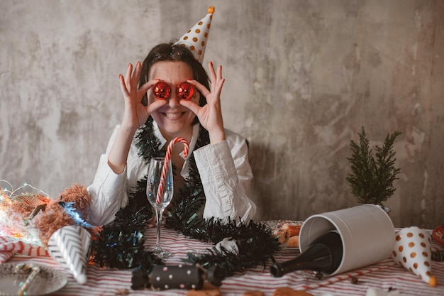 Jonge vrolijke vrouw in feestelijke feestmuts die haar ogen komisch bedekt met glanzende kerstbubbels